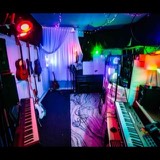 Wide view of the Studio San Francisco live room: guitars on the wall, two keyboards, an upright piano and modular curtains under string lights