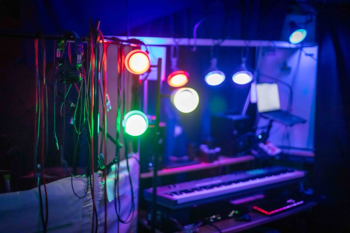 RGB accent lights on the overhead bar at Studio San Francisco, with monitoring headphones and cables hanging above a synth and laptop