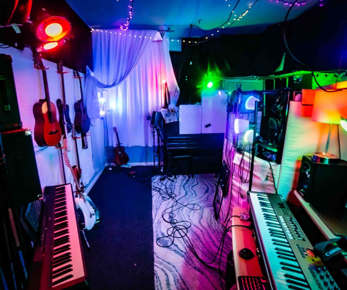 Wide view of the Studio San Francisco live room: guitars on the wall, two keyboards, an upright piano and modular curtains under string lights